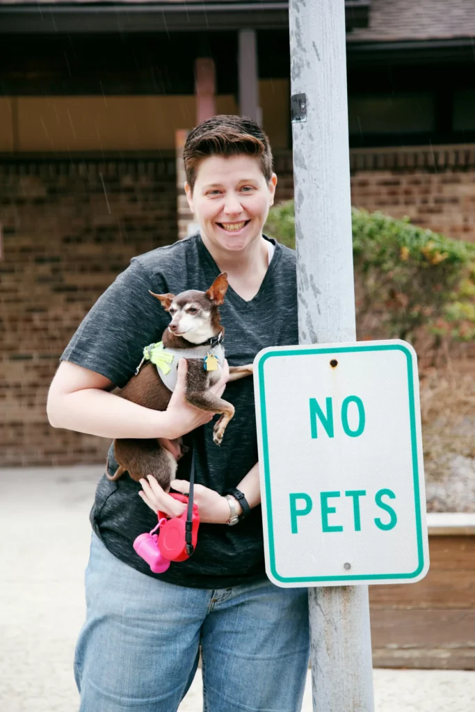 person holding a dog in front of a "no pets" sign to represent being disliked after religious deconstruction