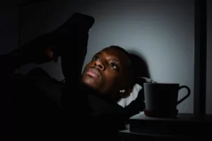 image of man looking at phone in bed in the dark to represent environmental related anxiety and insomnia